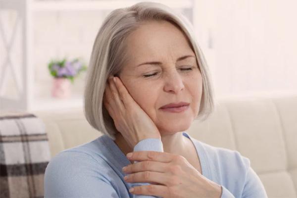 Mujer mayor con una mano en la oreja con una expresión de dolor.